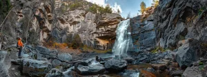 a solitary explorer gazes in awe at a majestic waterfall cascading down rugged cliffs in a remote, untouched wilderness.